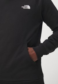 Sweatshirt noir avec des poignets et un ourlet côtelés, arborant un logo blanc sur la poitrine. Le matériau semble doux avec une texture lisse.