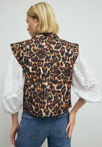 Luipaardprint vest met een gestructureerd ontwerp, voorzien van een geborduurd textuur, zwart en oranje kleuren, en witte oogjes puffmouwen.