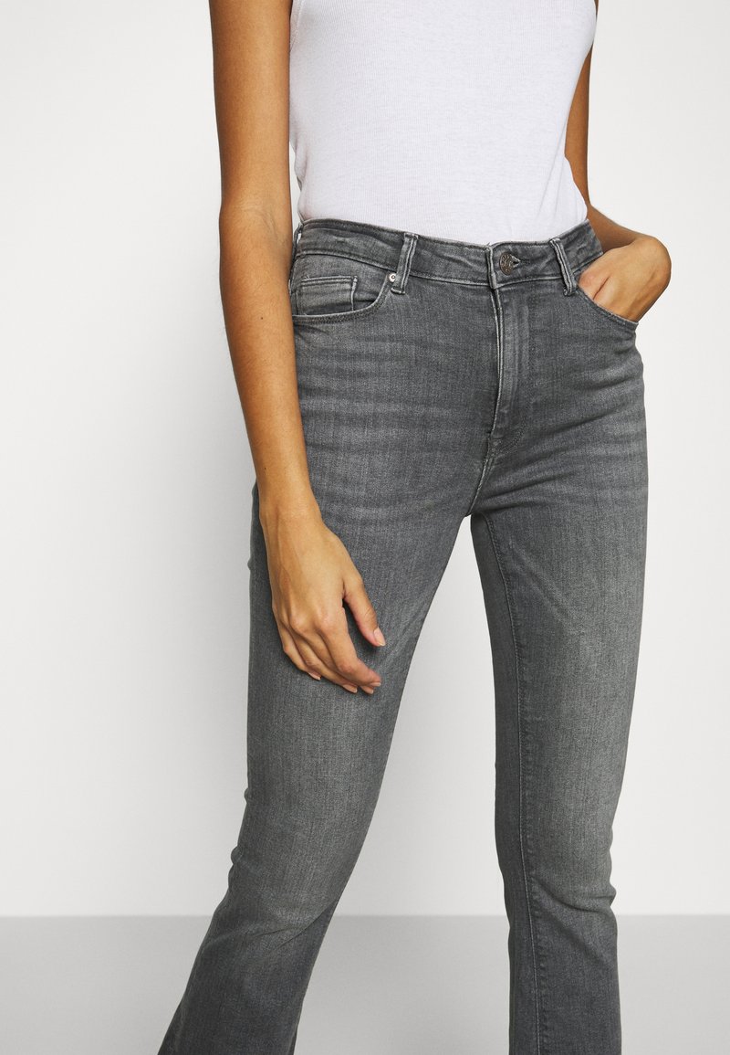 Graue Denim-Jeans im Slim-Fit, mit mittelhohem Bund, fünf Taschen und subtilen Auswaschungen an den Oberschenkeln, kombiniert mit einem weißen Tanktop.