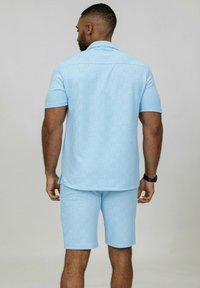 Ensemble décontracté bleu clair comprenant une chemise à col et à manches courtes, ainsi que des shorts assortis, tous deux fabriqués dans un tissu texturé avec des détails de couture visibles.