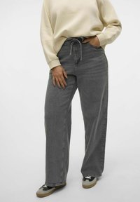 Jeans a gamba larga in denim grigio scuro, con vita regolabile e una leggera texture. Abbinati a una felpa crema e scarpe da ginnastica.