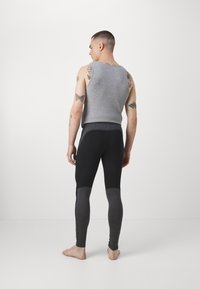 Szary top na ramiączkach z szerokimi paskami, zestawiony z czarnymi legginsami z ciemnoszarym panelem na dolnych nogawkach. Materiał wydaje się miękki i elastyczny.