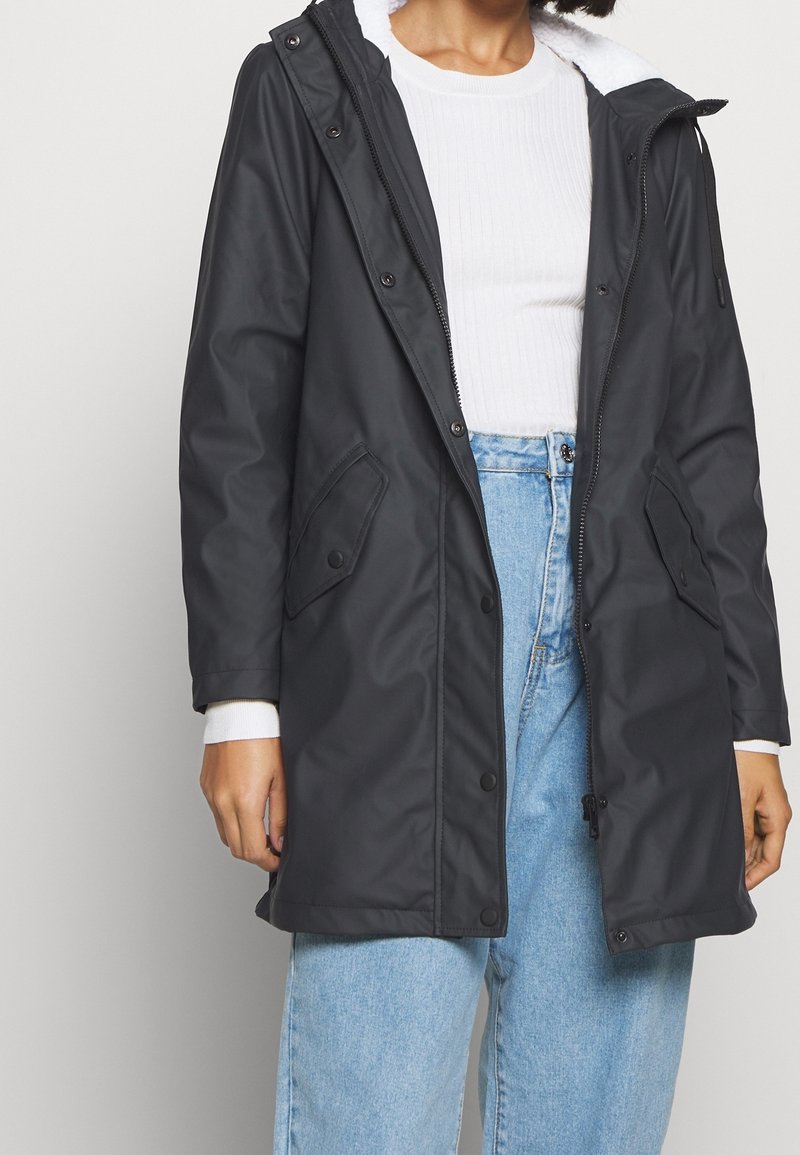 Svart vattenavvisande jacka med mjukt, vitt fleecefoder och huva. Har tryckknappsfickor och dragkedjestängning.