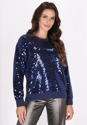 Pulover bleumarin cu paiete, cu guler rotund și mâneci lungi. Prezintă o suprafață texturată și mansete cu nervuri, asociat cu pantaloni metalici slim-fit.