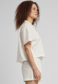 Hvit teksturert kortermet topp med avslappet passform og krage, parret med matchende shorts med strikk i livet.