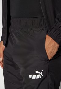 Schwarze Sporthose mit elastischem Bund, Seitentaschen und weißem Puma-Logo am unteren Bein. Glattes, leichtes Material mit matter Oberfläche.