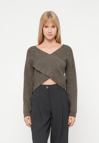 Heklet, v-hals, kort genser i mørkebrunt med en teksturert, kryssende frontdesign, kombinert med høy midje grå bukser.