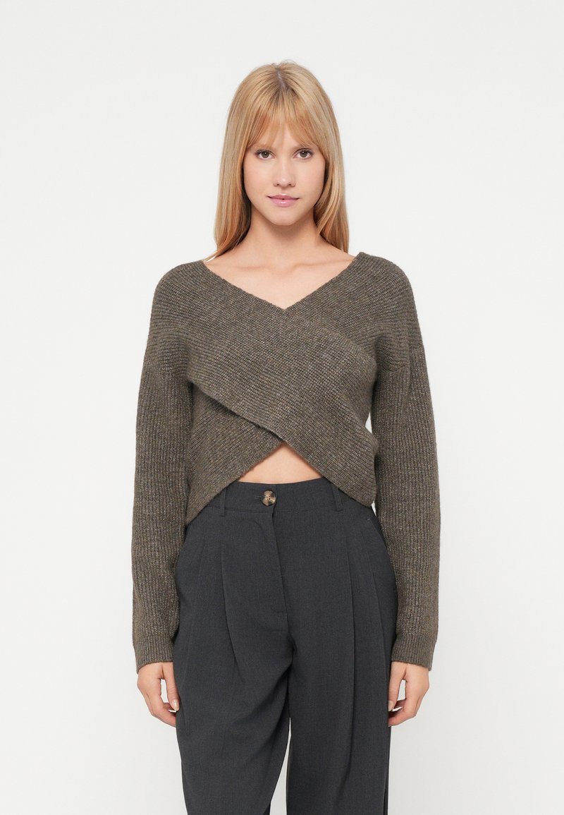 Heklet, v-hals, kort genser i mørkebrunt med en teksturert, kryssende frontdesign, kombinert med høy midje grå bukser.