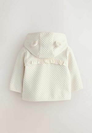 Balts quilting coats ar kapuci, ar ruffle akcentu gar muguru. Mīksta tekstūra un apaļas detaļas uz kapuces.