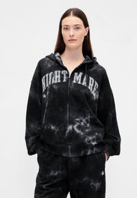 Casaco preto tie-dye com fecho de correr e a palavra "NIGHTMARE" delineada a branco no peito. Apresenta capuz com cordões e bolsos frontais.