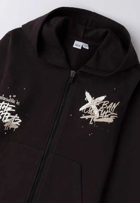 Felpa nera con zip e una morbida texture. Presenta un testo in stile graffiti metallico argento sul davanti e un grande cappuccio. Include tasche frontali.