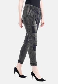 Slim-fit, mörkgrå byxor med slitningar, sidofickor och dekorativa nitar. Avsmalnande ben och uppvikta fållar framhäver designen.