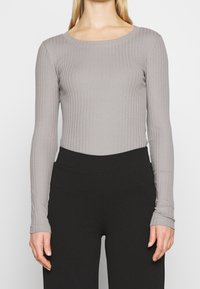 Maglia grigia a maniche lunghe con scollatura rotonda, tessuto texturizzato e design aderente, abbinata a pantaloni neri a vita alta.