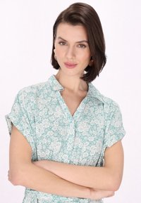 Abito camicia floreale verde chiaro con maniche ripiegate, colletto a bottoni e vestibilità rilassata, caratterizzato da un sottile motivo a fiori bianchi.