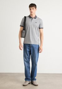 Γκρι πόλο μπλούζα με ανάγλυφη υφή και σκούρο γιακά, σε συνδυασμό με ανοιχτό μπλε τζιν και γκρι αθλητικά παπούτσια. Περιλαμβάνεται τσάντα ώμου.