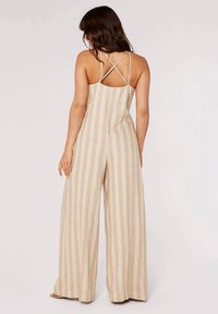 Beige- und cremefarbener gestreifter Jumpsuit mit lockerem Schnitt, der überkreuzte Träger am Rücken und weite Beinpartien aufweist. Die strukturierte Stofftextur verleiht dem Outfit Dimension.