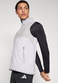 Pilka liemenė su užtrauktuku, turinti šviesiai pilką priekio skydelį, juodas rankoves ir tekstūruotą paviršių. Kairėje pusėje yra užsegama kišenė.