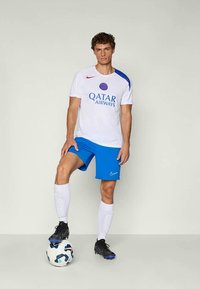 Bílý fotbalový dres Nike s modrými akcenty, se znakem "QATAR AIRWAYS". Modré šortky, černé kopačky a bílé ponožky. Fotbalový míč u nohou.