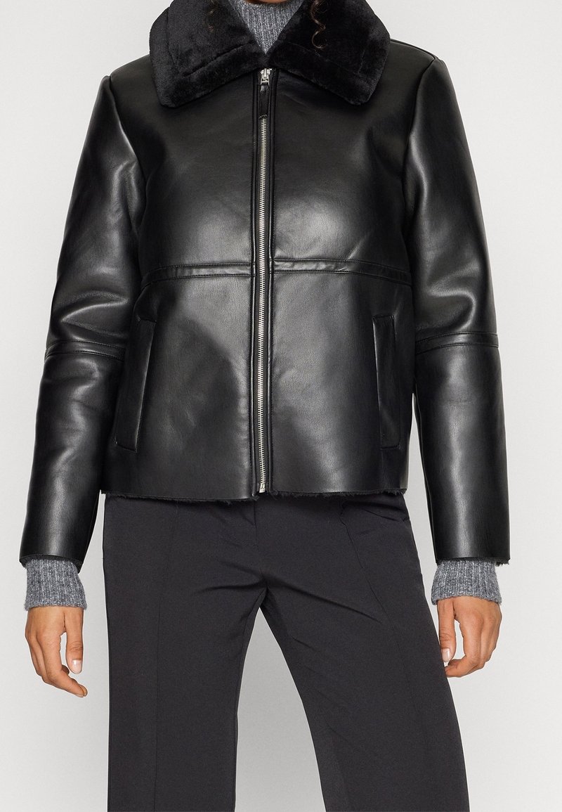 Veste en cuir noir avec un col en peluche noire, dotée d'une fermeture éclair à l'avant, de deux poches latérales et d'une coupe courte. Texture douce et finition lisse.
