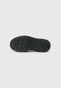 Black rubber shoe outsole with a textured, patterned surface featuring multi-directional treads for enhanced grip and durability.