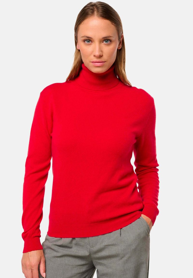 Pull en mailles côtelées rouge avec col roulé et manches longues. Texture lisse, forme ajustée et col haut. Associé à un pantalon gris.