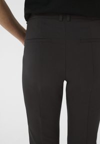 Black tailored pants featuring a smooth fabric, slim fit, and two back pockets with a subtle horizontal seam detail.