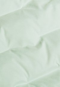 Hellgrüner Stoff mit glatter Textur, der feine Wellen und Falten aufweist und dadurch einen geschichteten Look mit weichem Finish schafft.