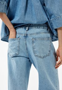 Pantalones vaqueros de denim azul claro con un corte relajado, que cuentan con dos bolsillos traseros, detalles de costura sutiles y un diseño de talle alto.