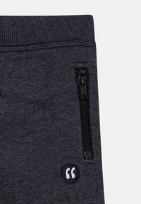 Donkergrijze sweatpants hebben een geribbelde tailleband, een ritszak aan de zijkant en een geborduurd rond accent met witte tekst.