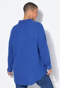 Niebieska, oversize koszula z guzikami, wykonana z teksturowanej tkaniny, z długimi rękawami i zaokrąglonym dołem. Posiada klasyczny kołnierz i guziki przy mankietach.