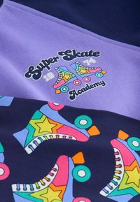Fialová a námořnická košile s grafikou kolečkových bruslí a hvězd v živých barvách. Obsahuje text "Super Skate Academy" v hravém písmu.
