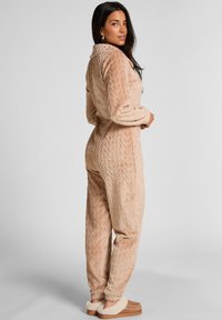 Svetlohnedý, mäkký fleece overal s textúrovaným vzorom listov. Obsahuje golier a manžety. Kombinovaný so svetlohnedými, kožušinou podšitými papučami.