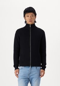 Black zip-up sweater with high collar, ribbed cuffs, and hem. Features a smooth texture and a fitted design. Paired with light blue jeans.