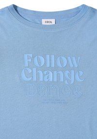 T-shirt bleu clair à col rond avec texte en relief "Follow Change Dance" et texte plus petit "Live your own life pursue your own way" sur le devant.