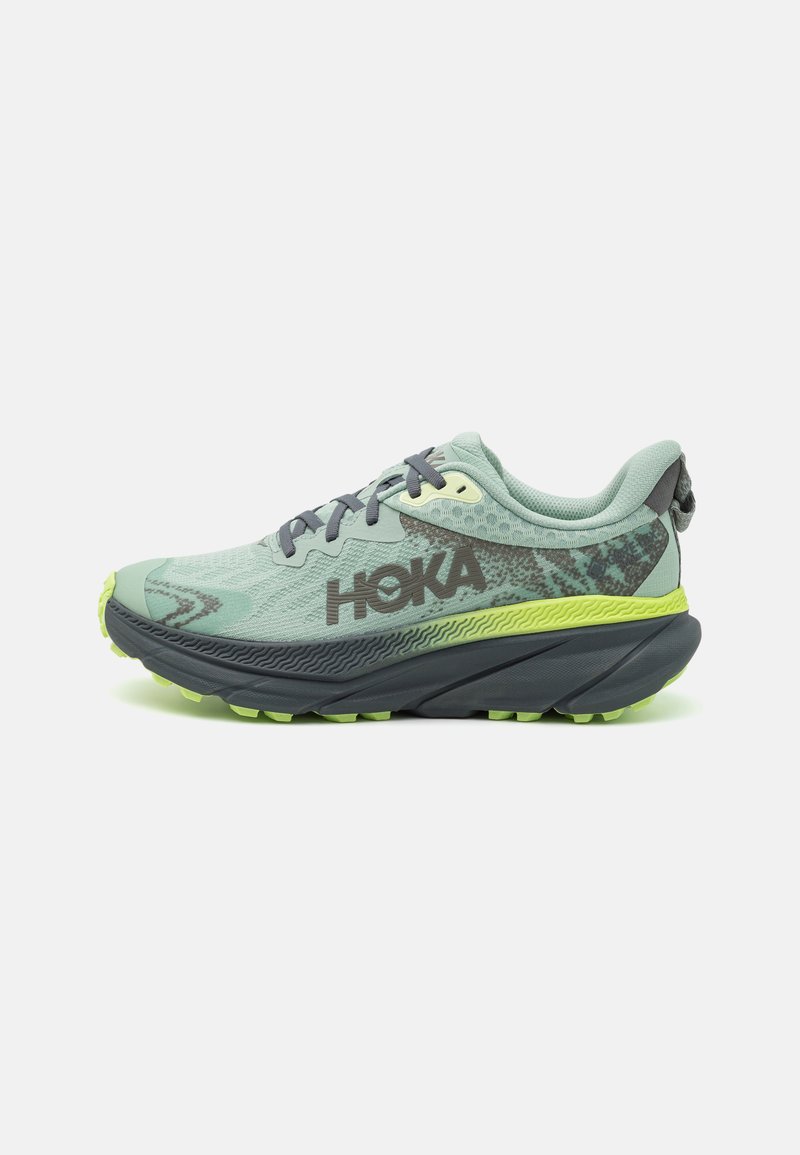 La chaussure de course HOKA présente une tige en maille vert clair, des accents gris foncé, une semelle intermédiaire rembourrée et une semelle extérieure en caoutchouc texturé avec des crampons de traction verts.