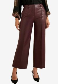 Burgunderfarbene Fake-Leder-Hosen mit weitem Bein, versehen mit genähten Vorderteilen und goldenen Knopfdetails, kombiniert mit schwarzen High Heels.
