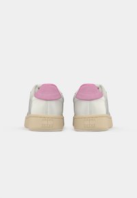 Vita sneakers med beige sulor och rosa hälflikar, sedd bakifrån, med "Tommy Jeans"-logotyp på sulorna.
