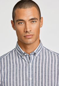 Camicia colletto con strisce verticali blu e bianche. Realizzata in lino, con chiusura a bottoni e un tessuto dalla texture particolare.