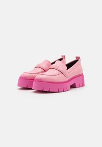 Des mocassins plateformes épais en rose clair et vif avec des semelles texturées et une sangle sur le dessus, présentés sur un fond blanc.