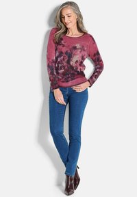 Langarm-ensenfarbiger Pullover mit floralen Muster, kombiniert mit blauen skinny Jeans und braunen, schulterhohen Stiefeln mit Absatz. Weicher Stoff und lässiges Design.