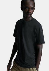 Sort crew-neck t-shirt lavet af glat stof, med kortærmer og en afslappet pasform. Kombineret med beige bukser.