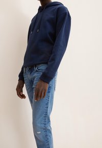 Námořnický modrý mikina s uvolněným střihem, kapucí na šňůrky a žebrovanými manžetami, v kombinaci se světle modrými džíny s odřeným vzhledem.