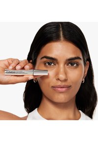 Gel per sopracciglia Clinique in un tubo argentato. La modella tiene il tubo vicino al viso, con una carnagione liscia e chiara e capelli scuri e lisci.