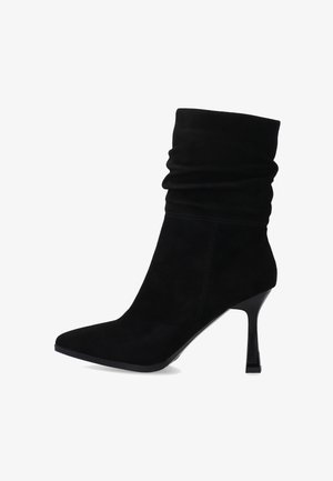 Czarne zamszowe botki za kostkę z luźną cholewką, spiczastym czubkiem i wysokim, błyszczącym obcasem typu szpilka. Gładka faktura z minimalnymi detalami szwów.