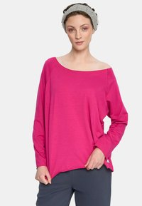 Fuksjowa bluzka z długim rękawem i konstrukcją odsłaniającą ramiona; miękki, lekki materiał; zestawiona z szarymi spodniami. Widoczne delikatne detale szwów.