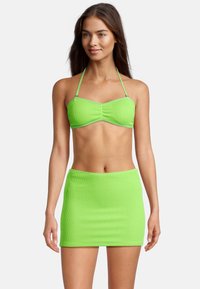 Maillot de bain bikini vert néon en tissu texturé, composé d'un haut bandeau et d'une mini-jupe assortie. Liens au niveau du cou et détails côtelés.