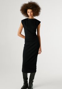 Abito midi nero con maniche corte, caratterizzato da un tessuto texturizzato e un colletto decorato. Indossato con stivali neri fino al ginocchio.