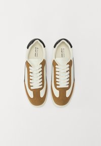 Baskets avec une tige en suède marron et en cuir blanc, un capuchon de talon noir et des lacets blancs. Bout arrondi et détails cousus.