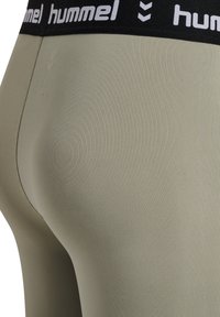 Nærbillede af olivengrønne leggings med sort taljebånd med hvide "hummel"-logoer og chevron-mønstre.