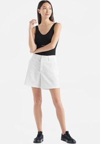 Body nero senza maniche con scollo a barca, abbinato a pantaloni corti bianchi a vita alta. Il modello indossa scarpe da ginnastica nere. Sfondo semplice.